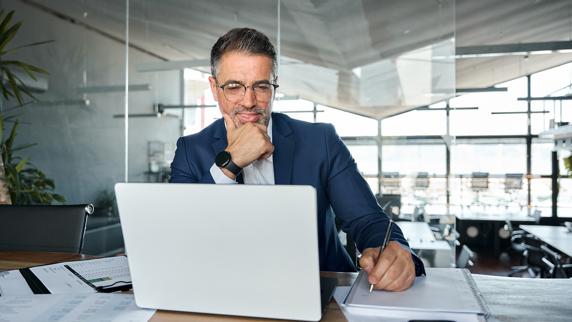 Middle aged man in a suit sitting at his desk smiling